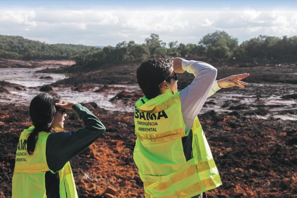 Two workers wearing fluorescent yellow vests look out over the catastrophic damage after the collapse of the Vale tailings dam in Brumadinho, Brazil.